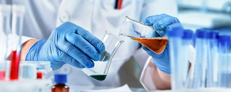 Scientist wearing blue gloves pouring chemical solutions in laboratory glassware during chemical testing and research